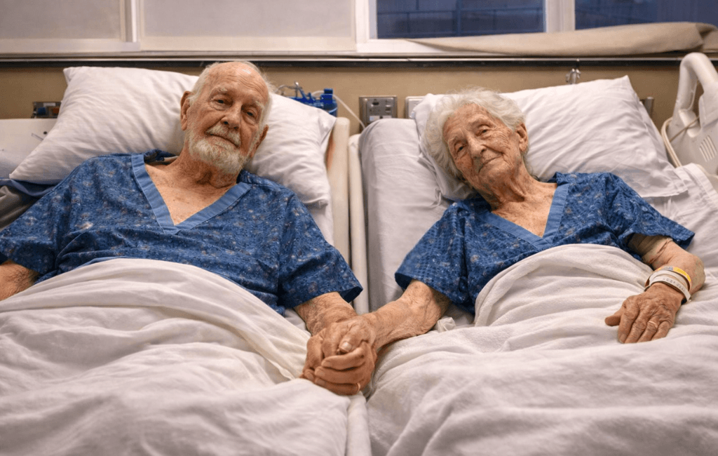 Elderly couple in hospital beds holding hands, representing aged care planning and financial considerations in Australia